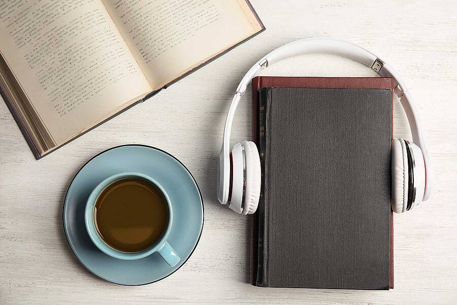 a photo looking straight down on a desk with an open book, a cup of coffee and a Bible with headphones around it