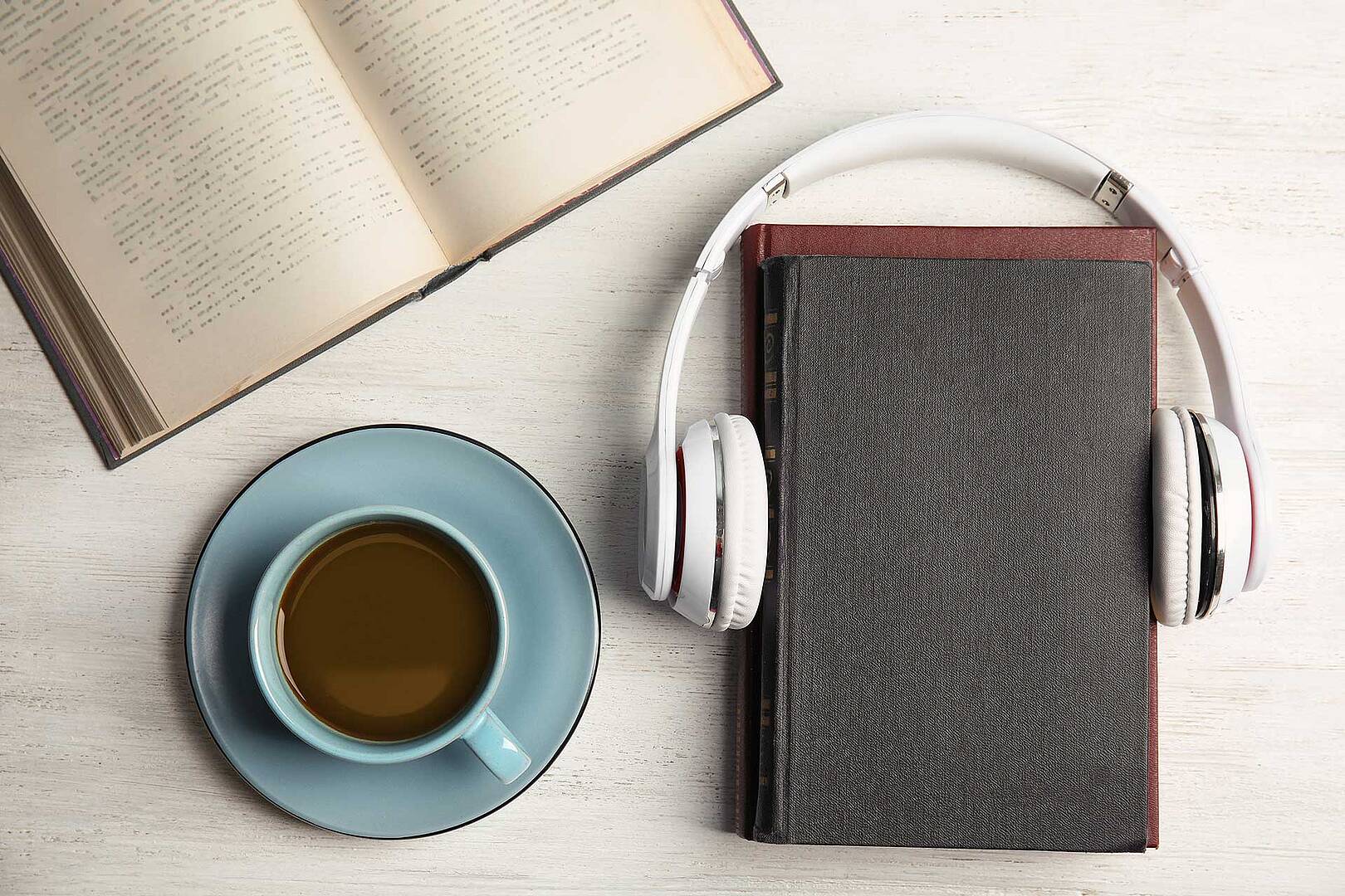 a photo looking straight down on a desk with an open book, a cup of coffee and a Bible with headphones around it