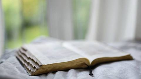 photo of an open bible on a blanket with a window in the background